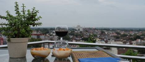 A table with a potted plant, two bowls of food, a glass of red wine, and a blue napkin on a balcony overlooking a cityscape.