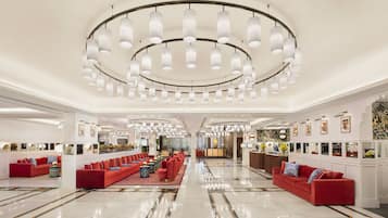 A spacious lobby with red sofas, a central coffee table, and a chandelier.