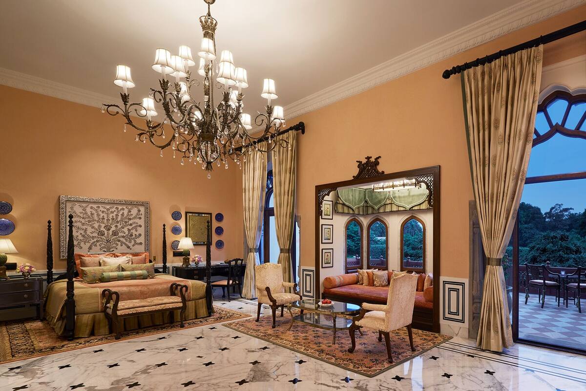 A spacious living room with a large chandelier, a comfortable sofa, a dining area, and a view of the outdoors through large windows.