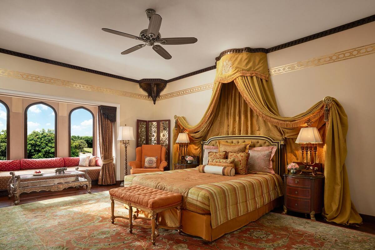 A luxurious bedroom with a four-poster bed, ornate curtains, and a large window with a view of greenery.