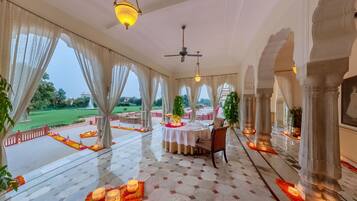 A spacious indoor area with a dining setup, large windows, and a view of a garden.