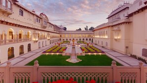 A courtyard with a central fountain, surrounded by symmetrical flower beds and a well-maintained lawn.