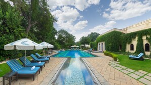 A pool area with lounge chairs and umbrellas, surrounded by greenery and a building with ivy-covered walls.