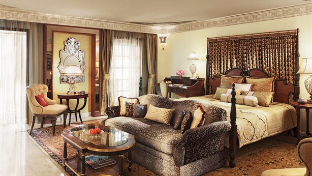 A spacious hotel room with a large bed, a sofa, a desk, and a chair.