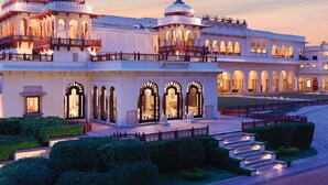 A grand, illuminated building with multiple domes and arched windows, featuring a spacious courtyard and well-maintained gardens.