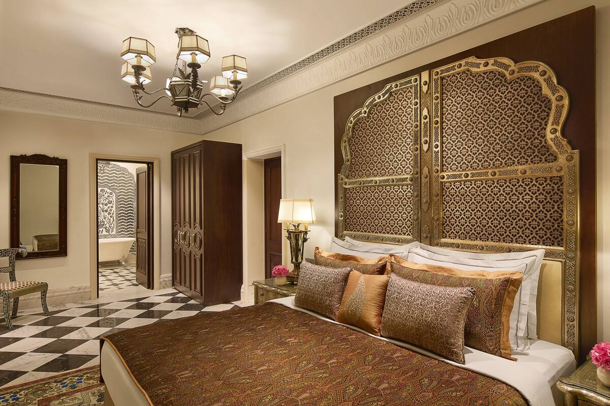 A luxurious bedroom with a large bed, ornate headboard, and a chandelier.