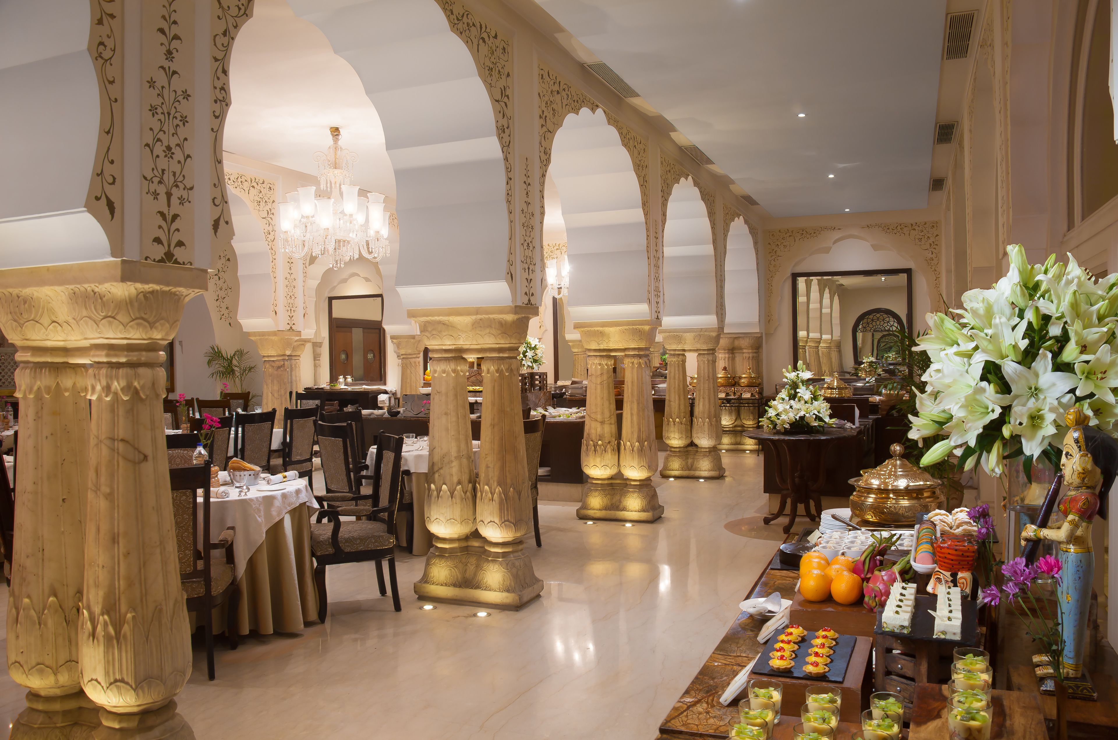 Uma área de refeições luxuosa com colunas decorativas, lustres e diversas opções de comida.