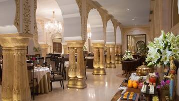 Uma área de refeições luxuosa com colunas decorativas, lustres e diversas opções de comida.