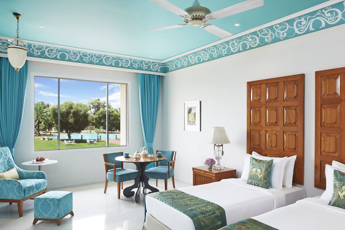 A hotel room with a large window, a ceiling fan, a wooden door, and a small table with chairs.