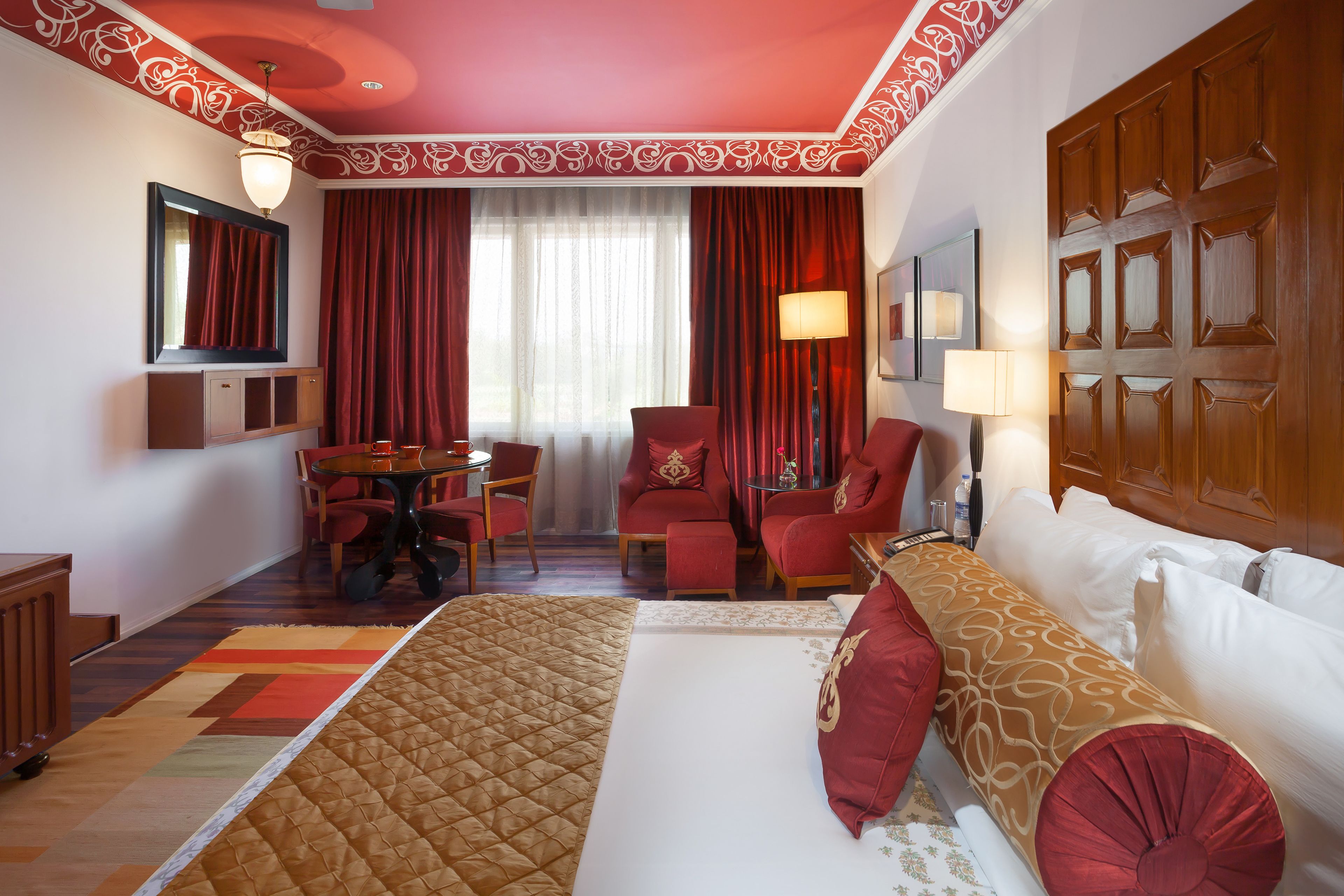 A hotel room with a large bed, a desk, two chairs, a table, and a wardrobe.