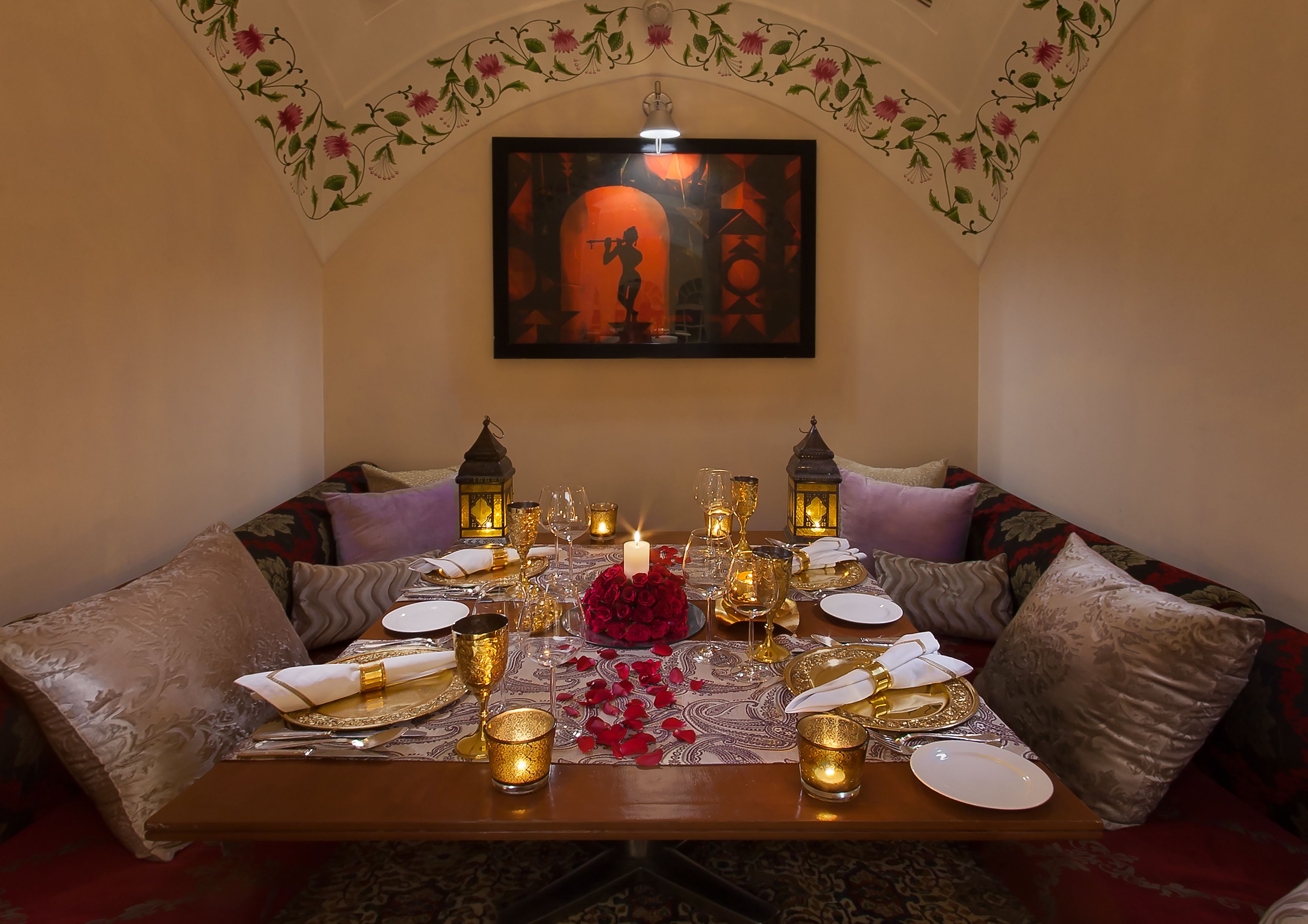A dining area with a table set for two, featuring a candle centerpiece, two lanterns, and a framed artwork above.