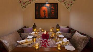 A dining area with a table set for two, featuring a candle centerpiece, two lanterns, and a framed artwork above.