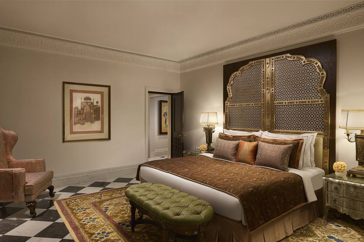 A classic bedroom with a large bed, a green bench, a patterned rug, and a framed picture on the wall.
