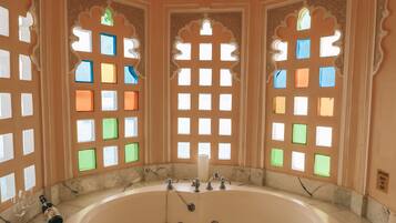 Una bañera grande y redonda en una habitación con ventanas ornamentales y un candelabro.