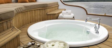 Una terrazza in legno con una vasca idromassaggio, una panchina di legno e una ciotola piena di fiori.