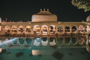 Une vue nocturne d’un hôtel avec une grande piscine qui reflète l’architecture du bâtiment.