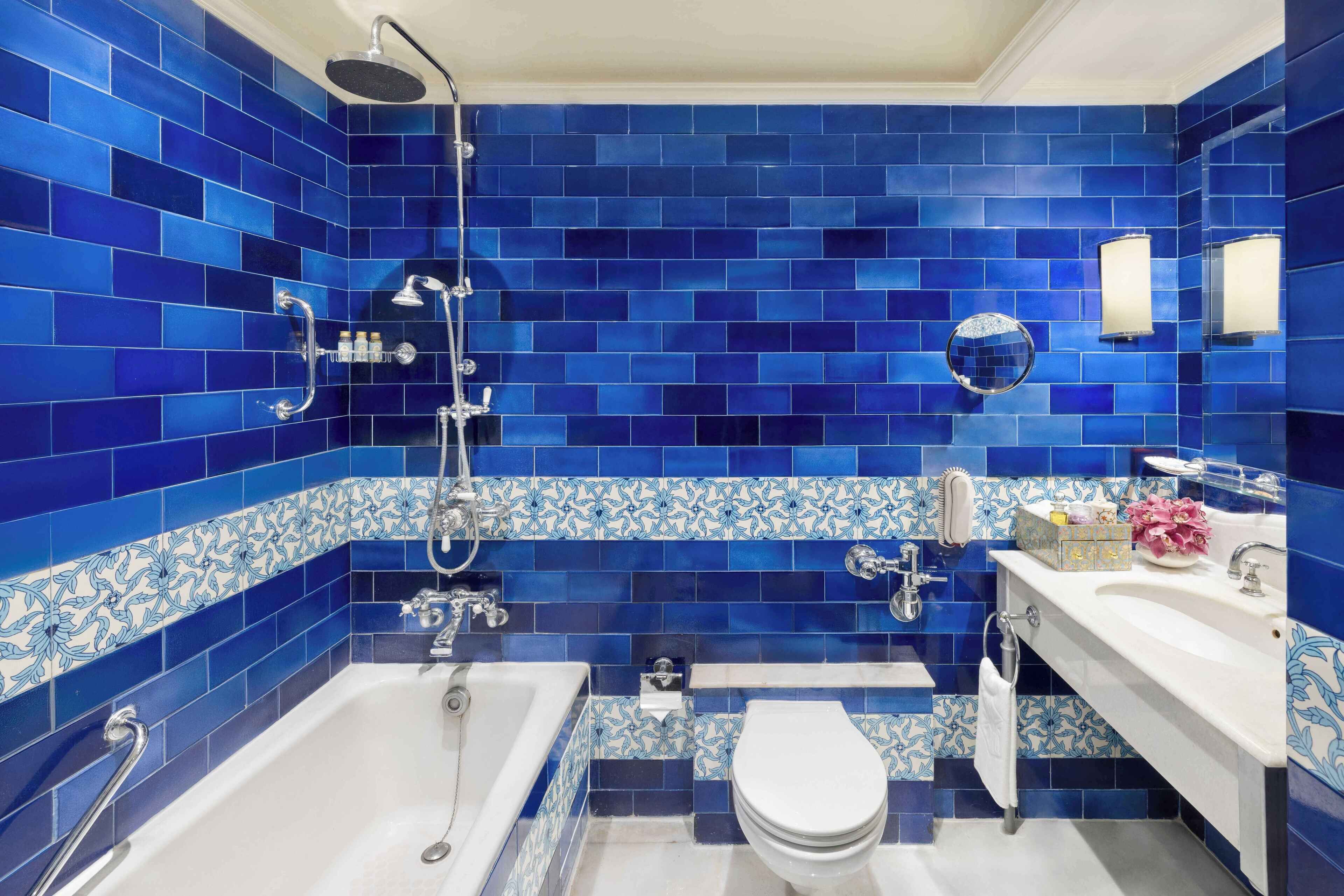 A bathroom with blue-tiled walls, a white bathtub, a white toilet, and a white sink with a mirror.