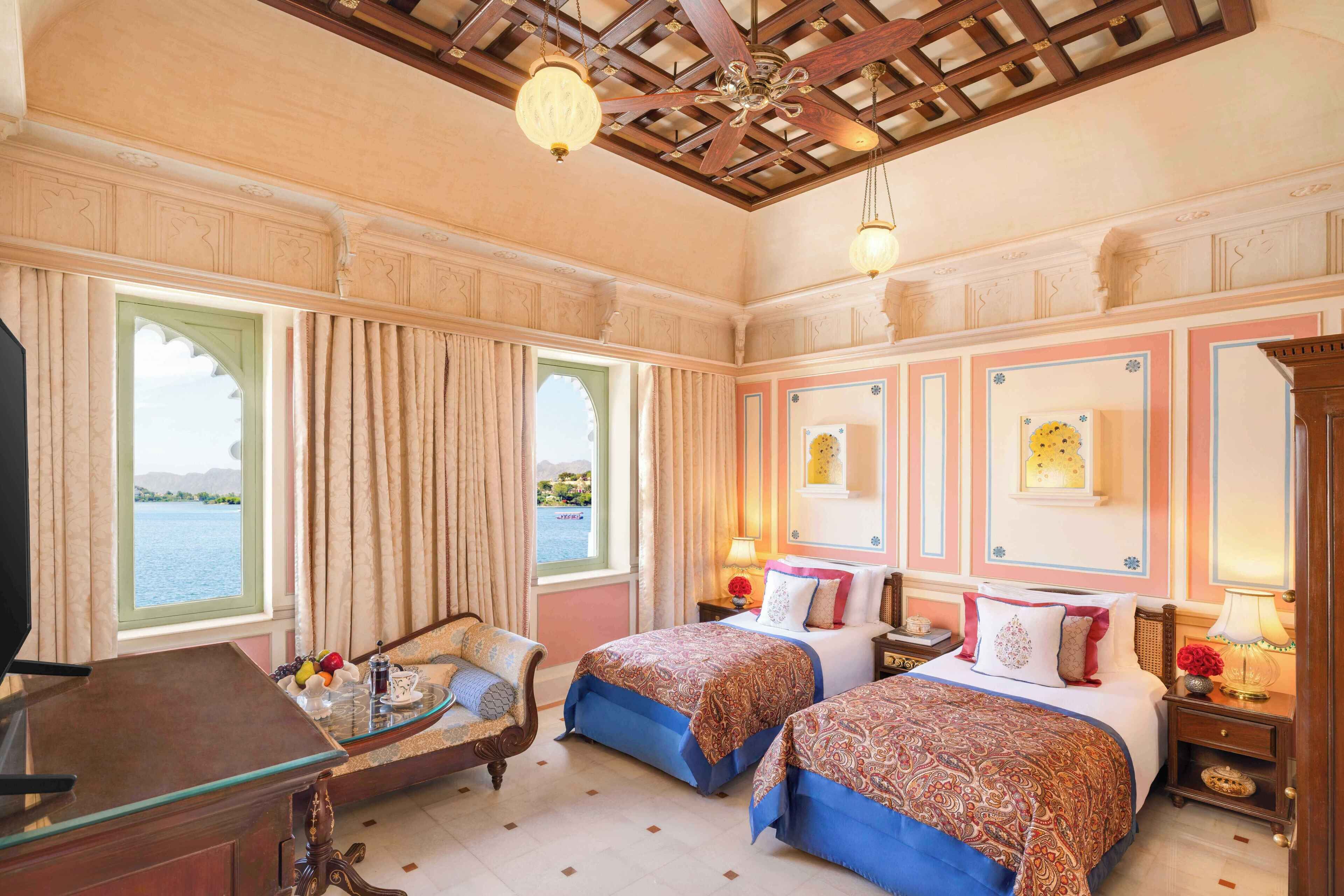 A hotel room with two beds, a desk, a chair, and a view of a body of water through large windows.