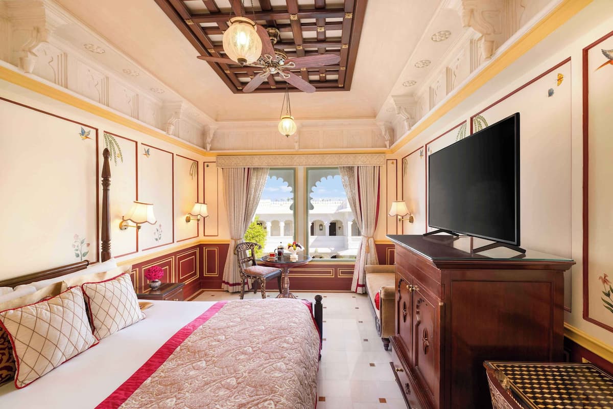 Ein Hotelzimmer mit einem großen Bett, einem Fernseher, einem Schreibtisch mit Lampe und Blick ins Freie durch das Fenster.