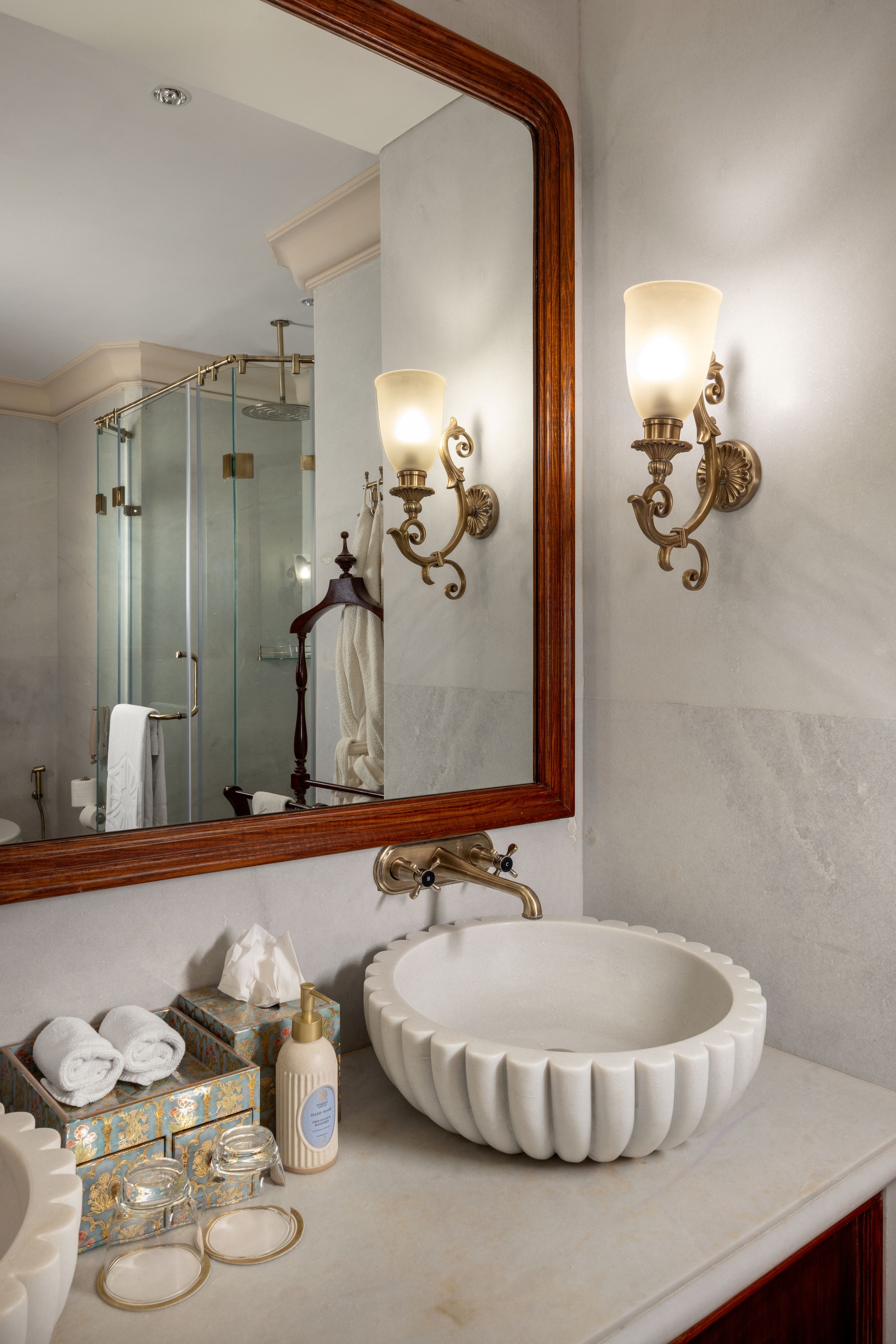 A bathroom with a large mirror, two wall-mounted lights, a white sink, and a glass shower enclosure.