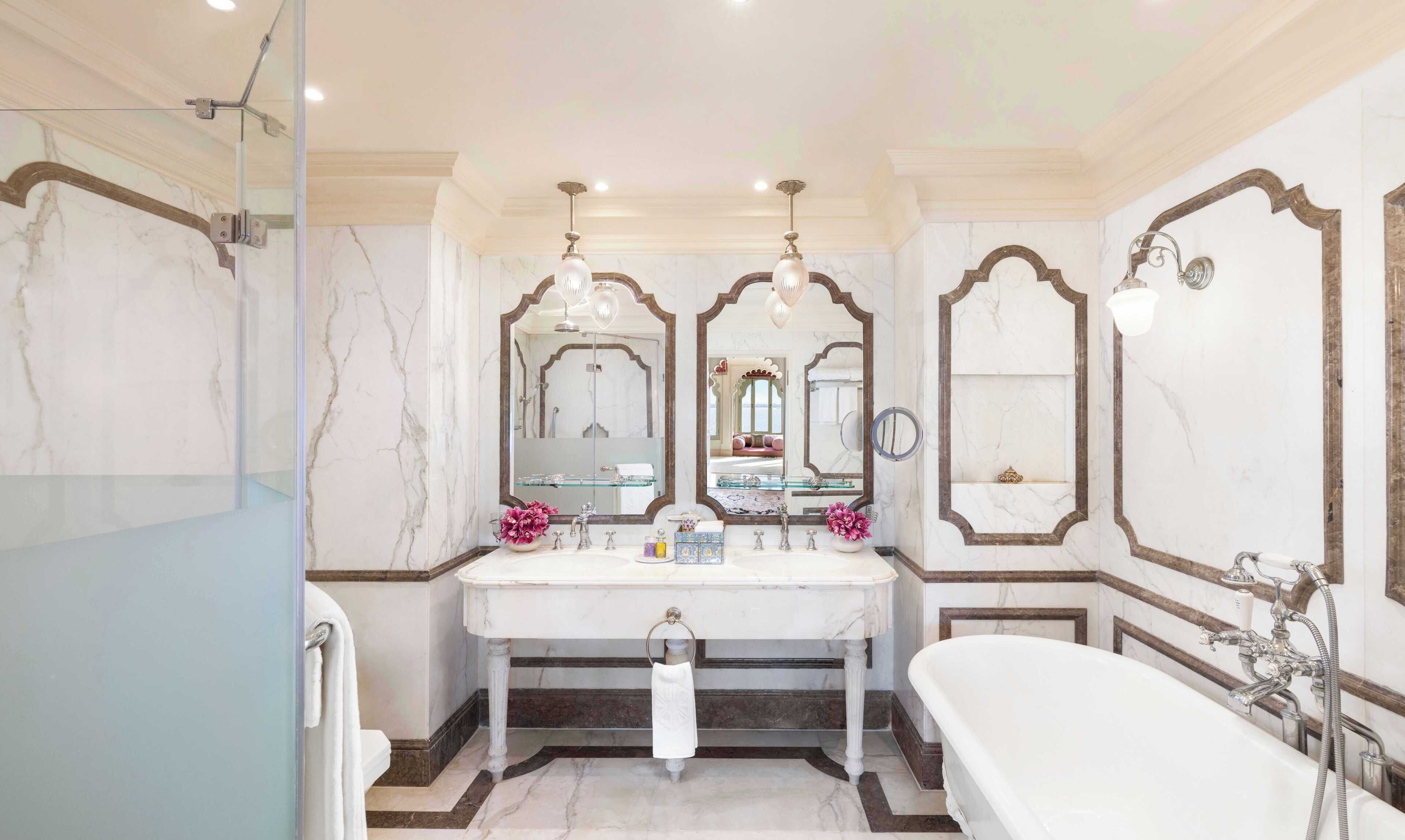 Une salle de bain luxueuse avec un grand meuble-lavabo en marbre, une baignoire sur pieds et des miroirs décoratifs.