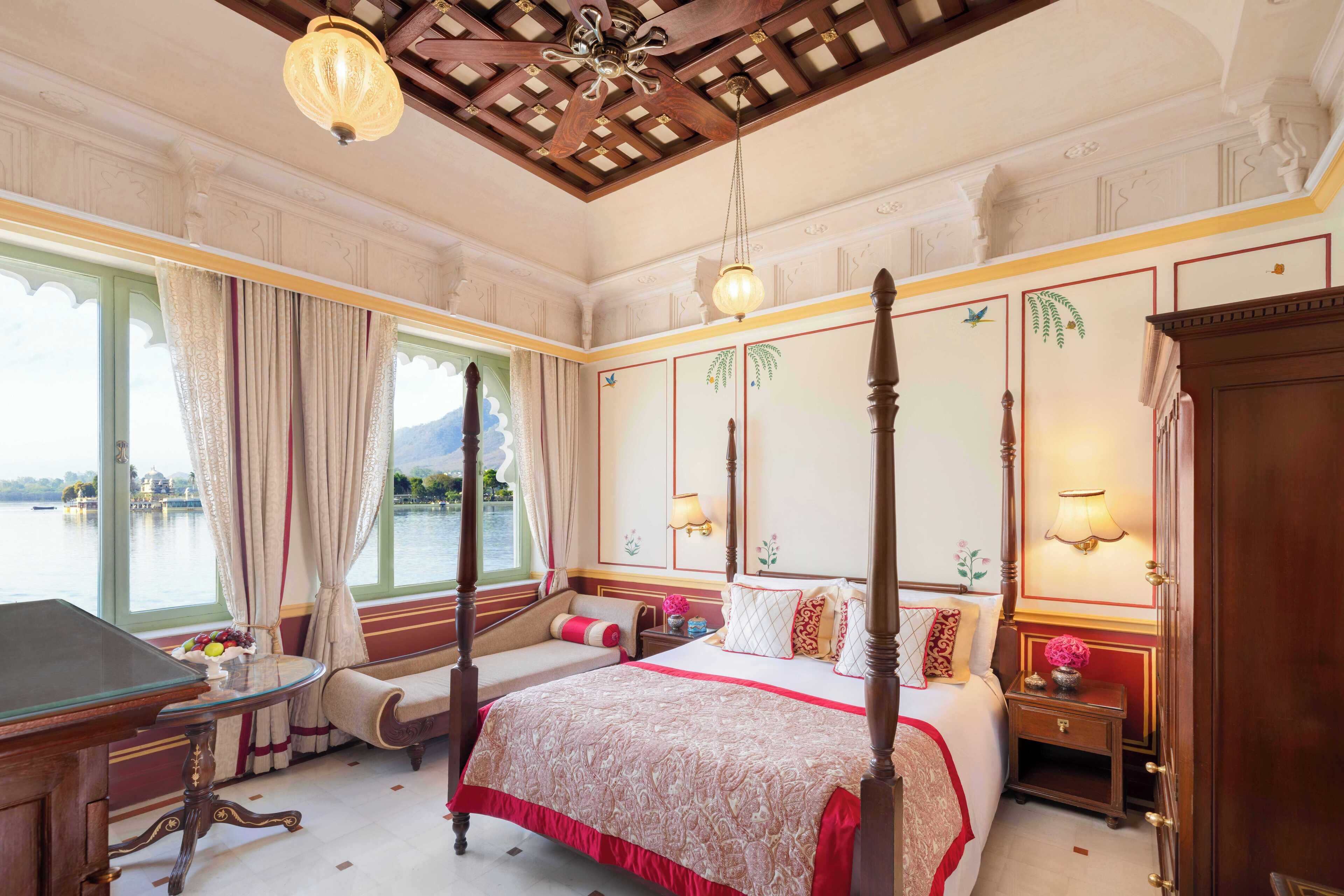 A luxurious bedroom with a four-poster bed, a wooden desk, and a view of a lake.