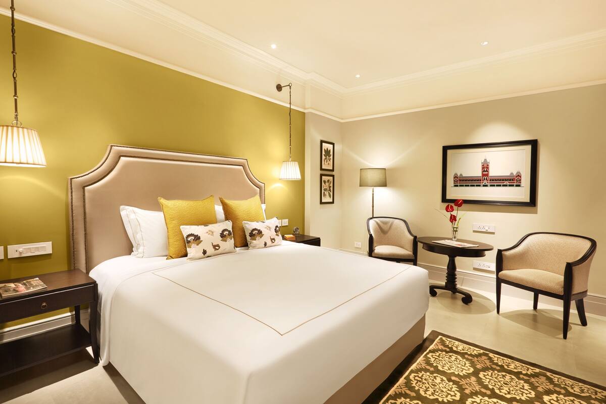A hotel room with a large bed, bedside tables, a chair, a small table, and a framed picture on the wall.