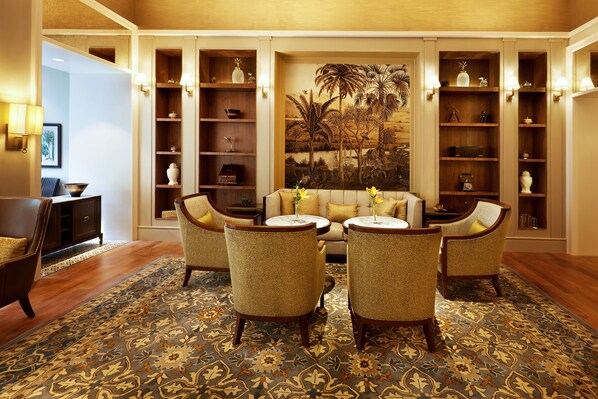 Una habitación con un sofá, cuatro sillones, una mesa de centro y un tapete estampado. Hay estantes con objetos decorativos y un cuadro grande en la pared.