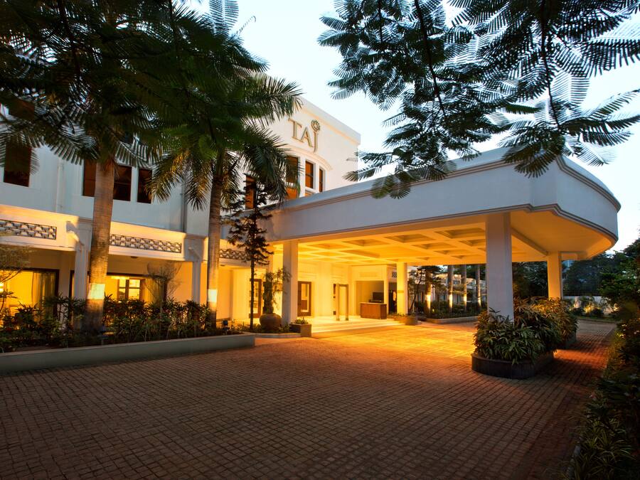 Entrada de un hotel con un corredor cubierto, palmeras y un área empaveda de ladrillo.
