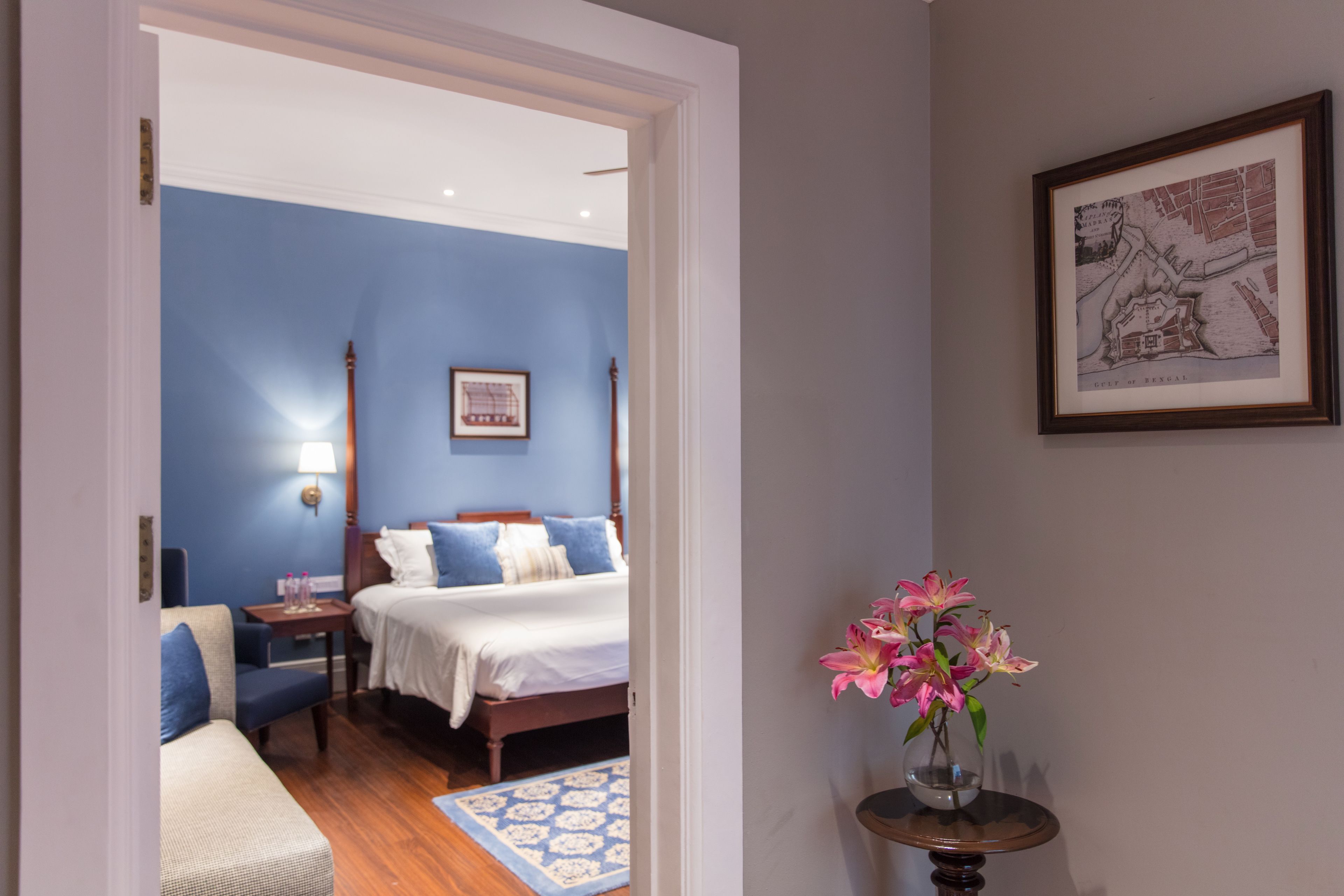 A bedroom with a bed, bedside table, lamp, and a vase with flowers.