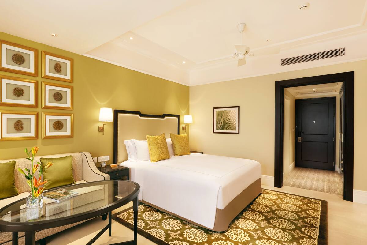 A hotel room with a large bed, a glass coffee table, a sofa, and a wall with framed artwork.