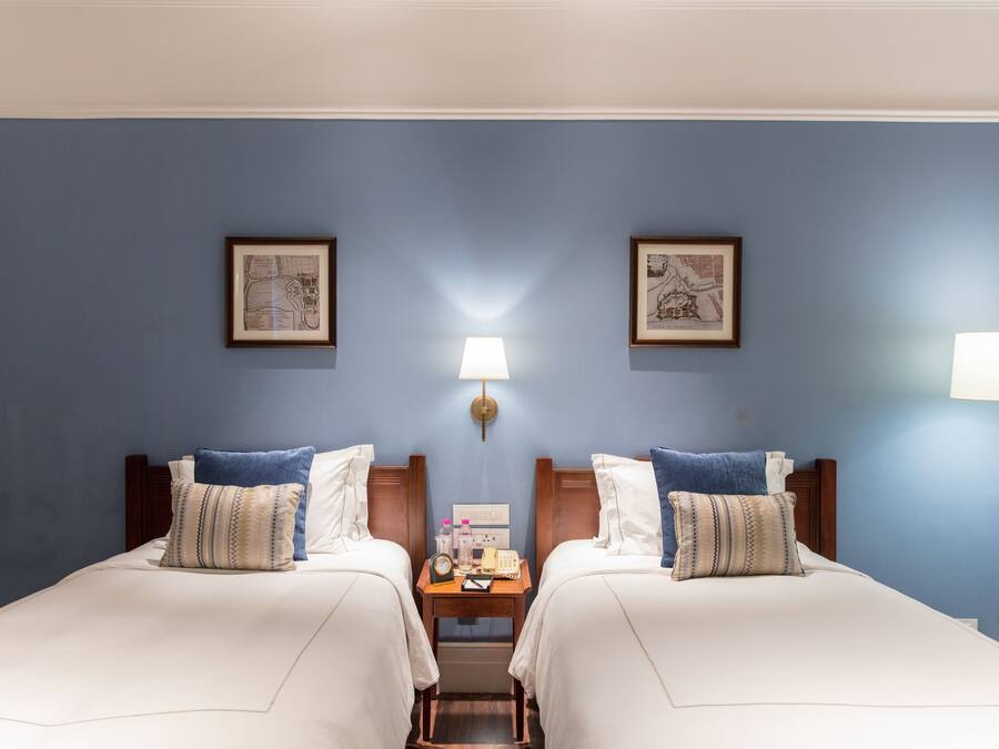 Habitación de hotel con dos camas, una mesita de noche, una lámpara y cuadros en las paredes.