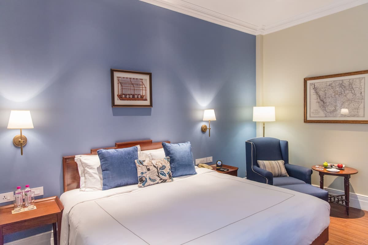 A hotel room with a large bed, two wall-mounted lamps, a chair, a small table with fruit, and a framed map on the wall.