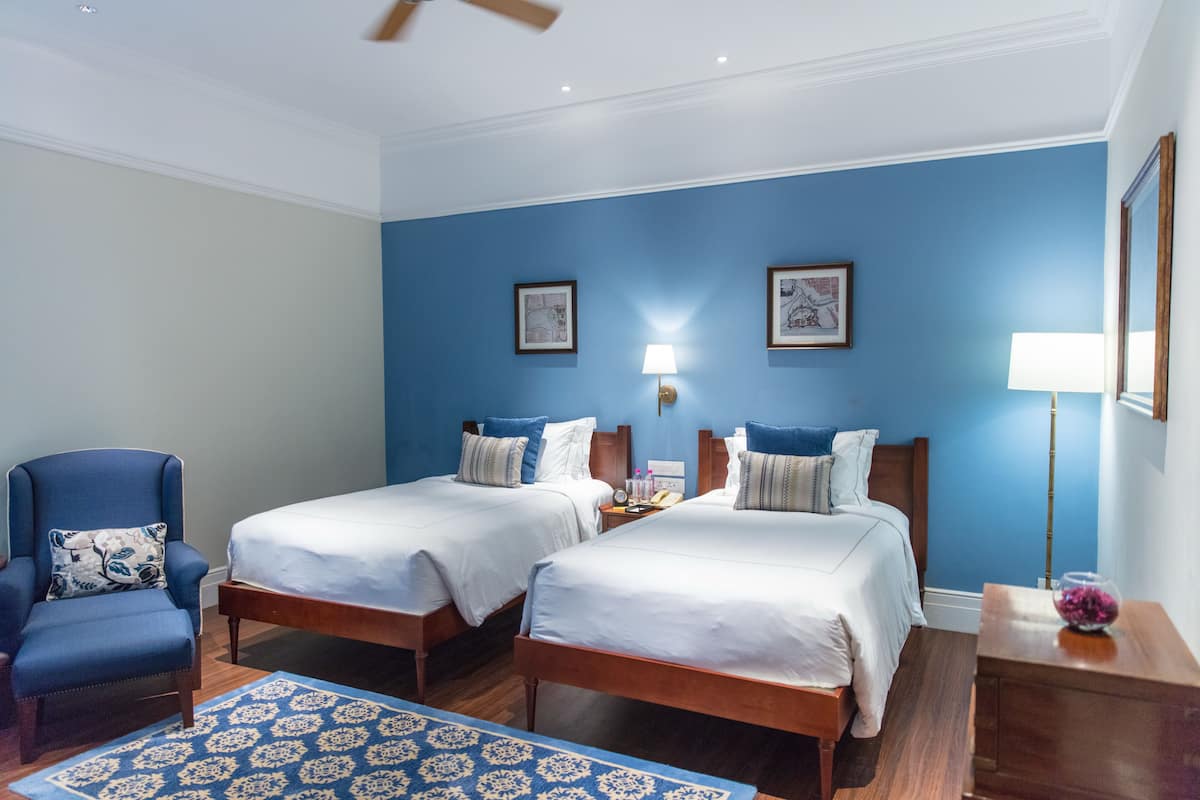 A hotel room with two beds, a chair, a lamp, and a picture frame on the wall.