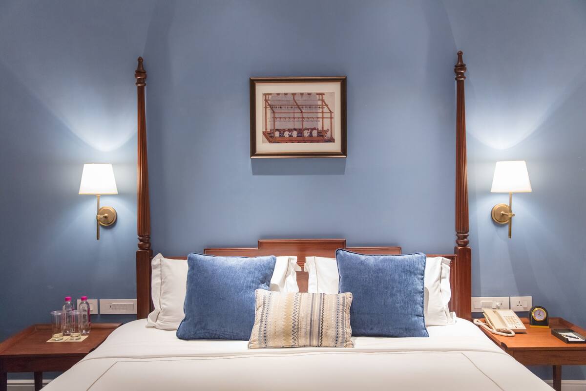 A neatly made bed with blue and white pillows, a framed picture on the wall, and bedside lamps on either side.