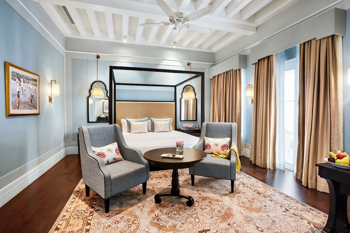 A hotel room with a large bed, two armchairs, a round coffee table, and a patterned rug.