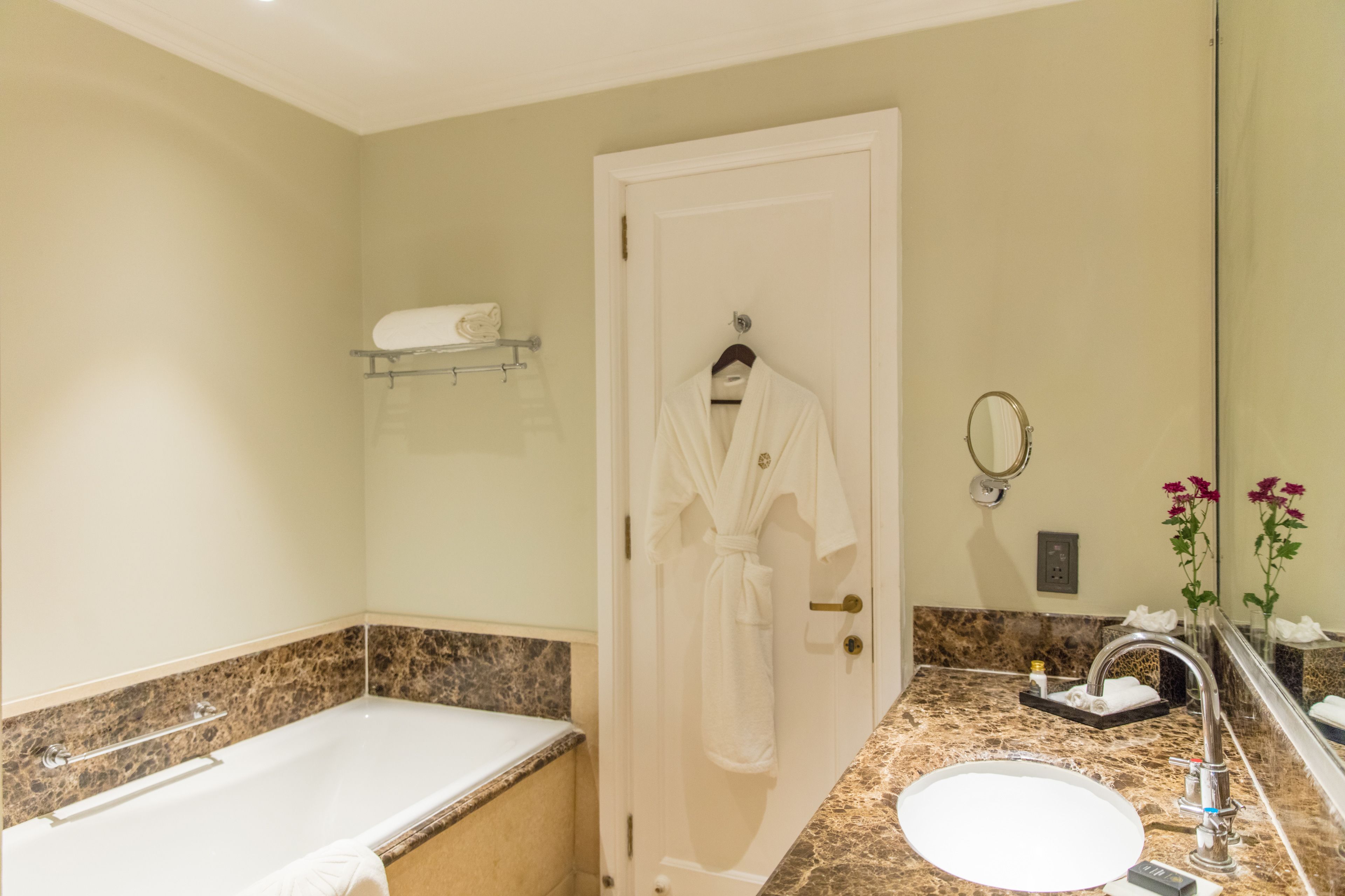 A bathroom with a bathtub, a sink, a mirror, and a robe hanging on a door.