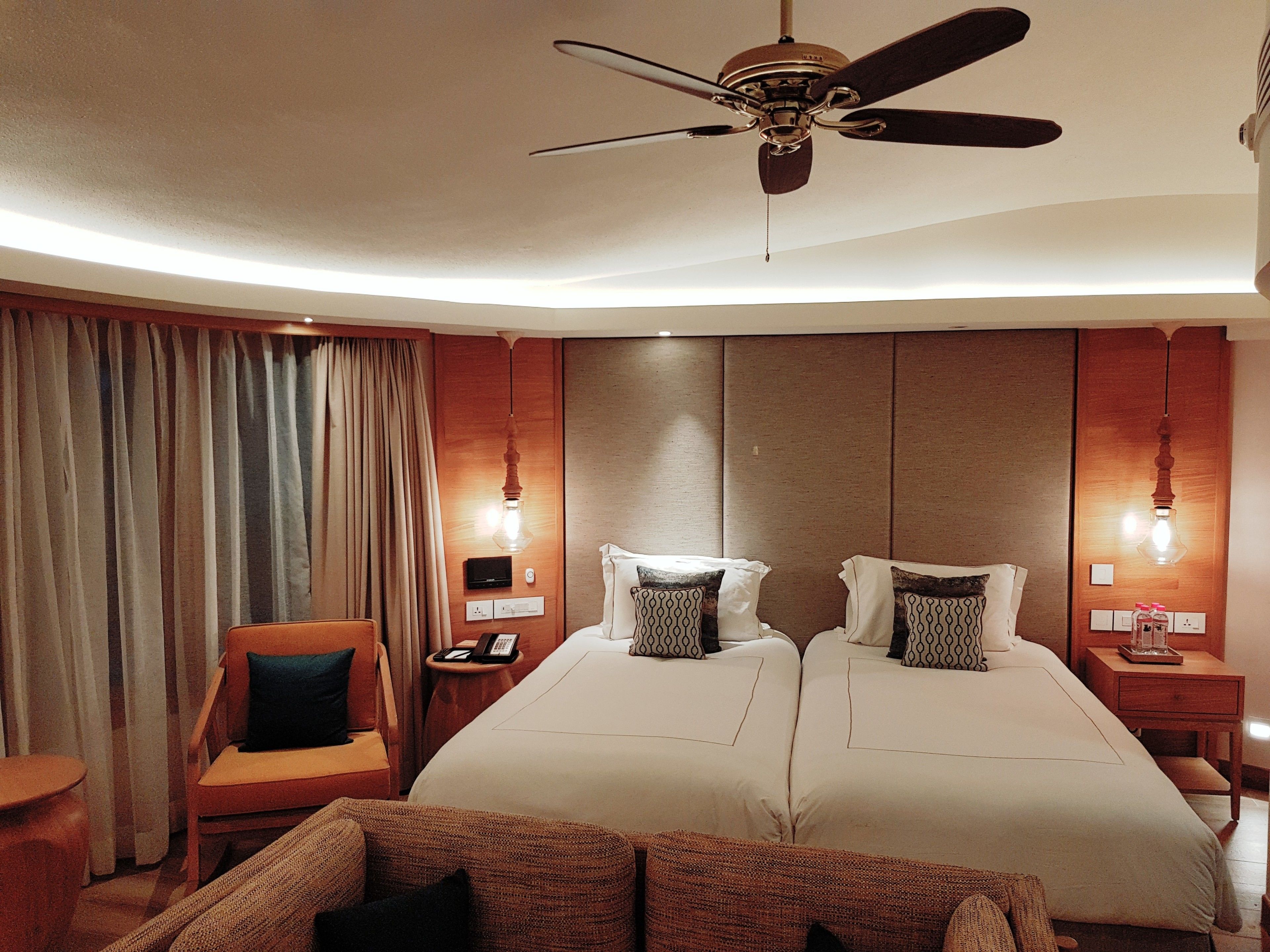 A hotel room with two beds, a ceiling fan, a desk with a phone, and a chair.