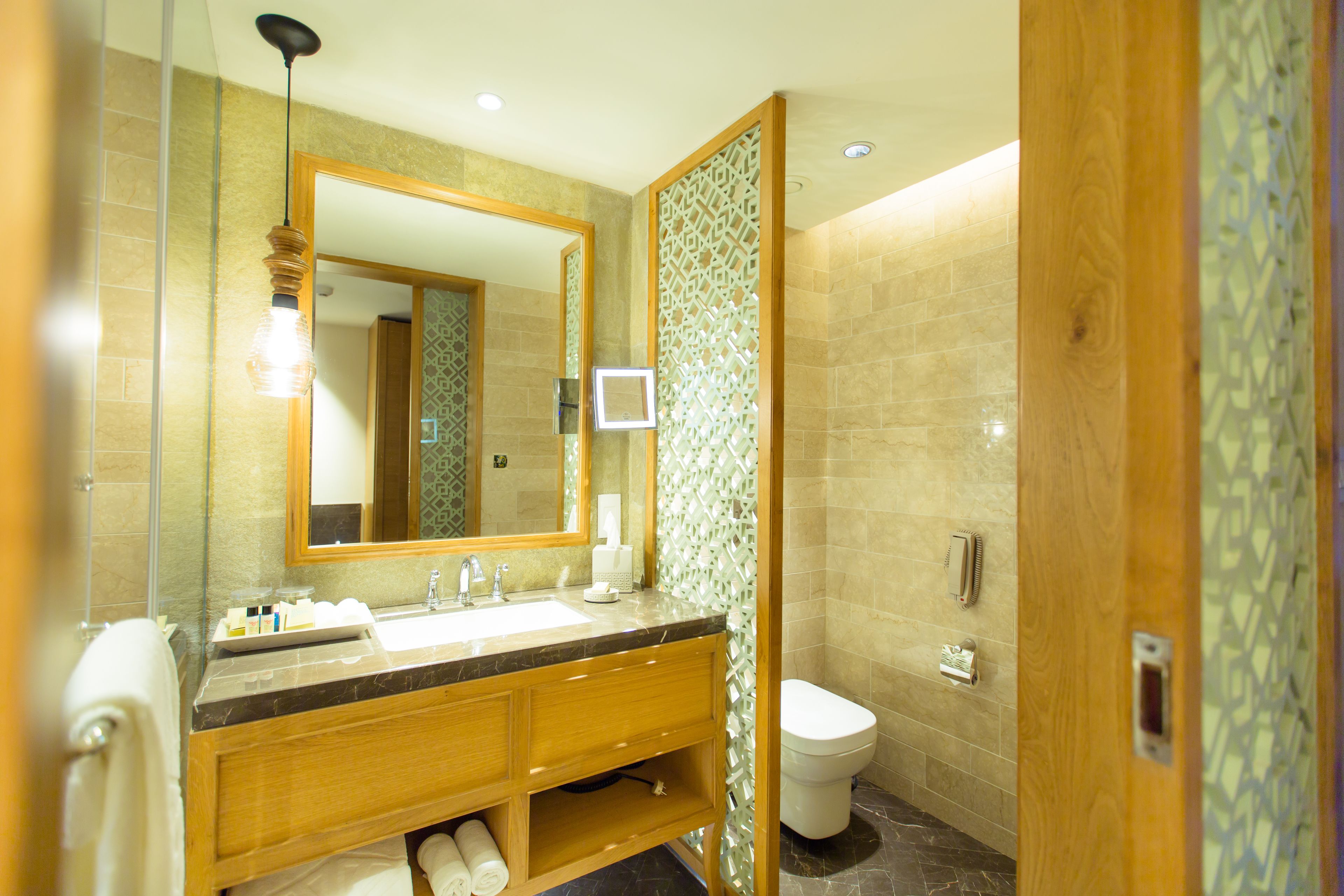 Un baño moderno con lavamanos de mármol, tocador de madera y un espejo grande.