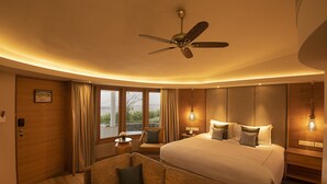 Hotelkamer met een groot bed, een plafondventilator, een bank, een nachtkastje en een raam met gordijnen.