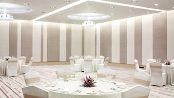 Un salón de banquetes con mesas redondas, sillas blancas y una araña.
