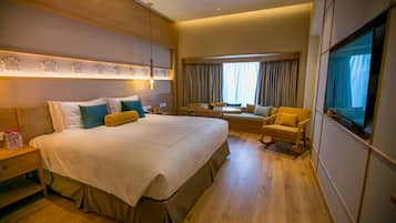 Habitación de hotel con una cama grande, una mesita de noche, una silla, un sofá y un televisor.