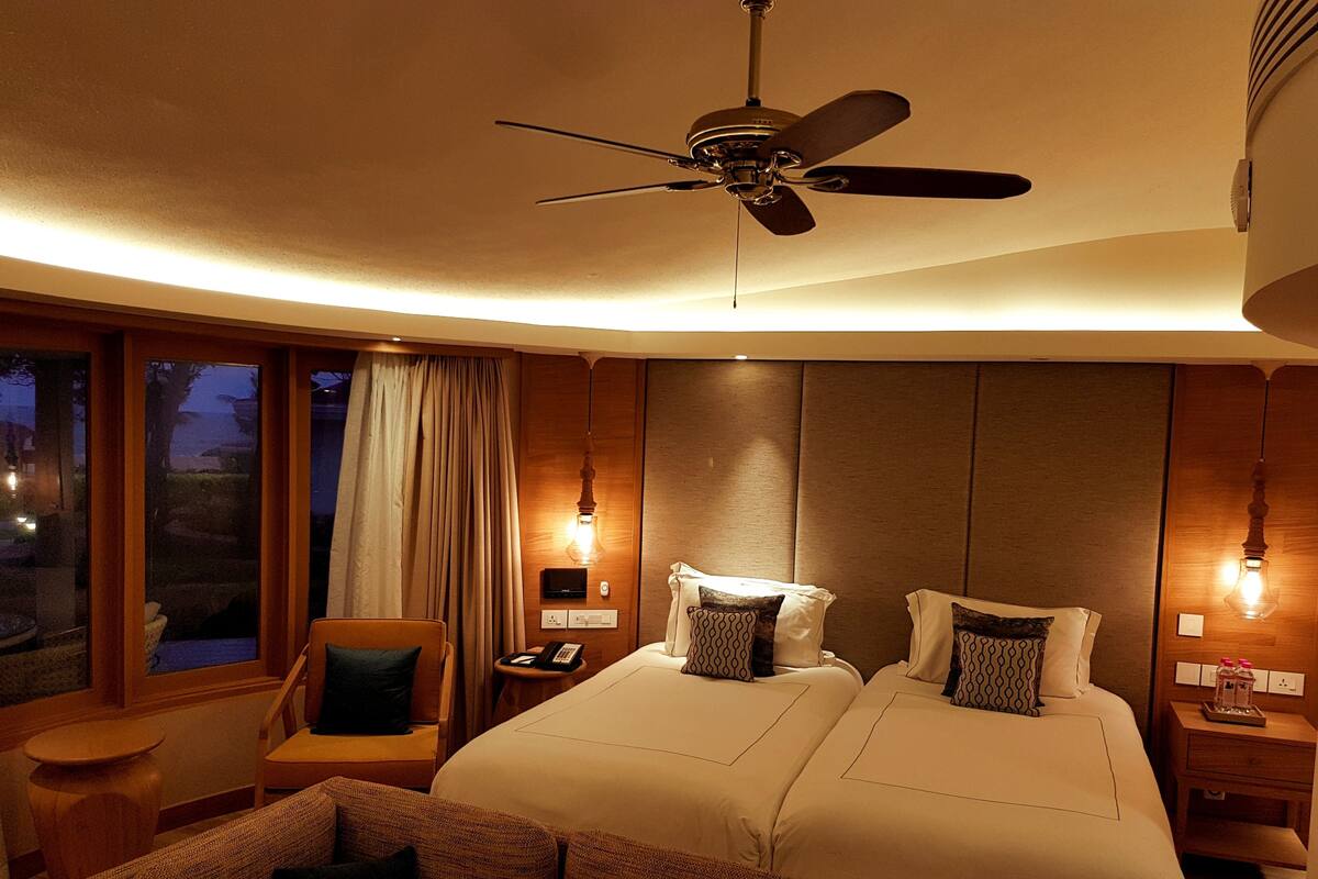 Habitación de hotel con dos camas, ventilador de techo, escritorio con teléfono y vistas al exterior.