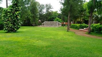 Une zone herbeuse bien entretenue, avec une structure en pierre au centre, entourée d’arbres et d’arbustes.