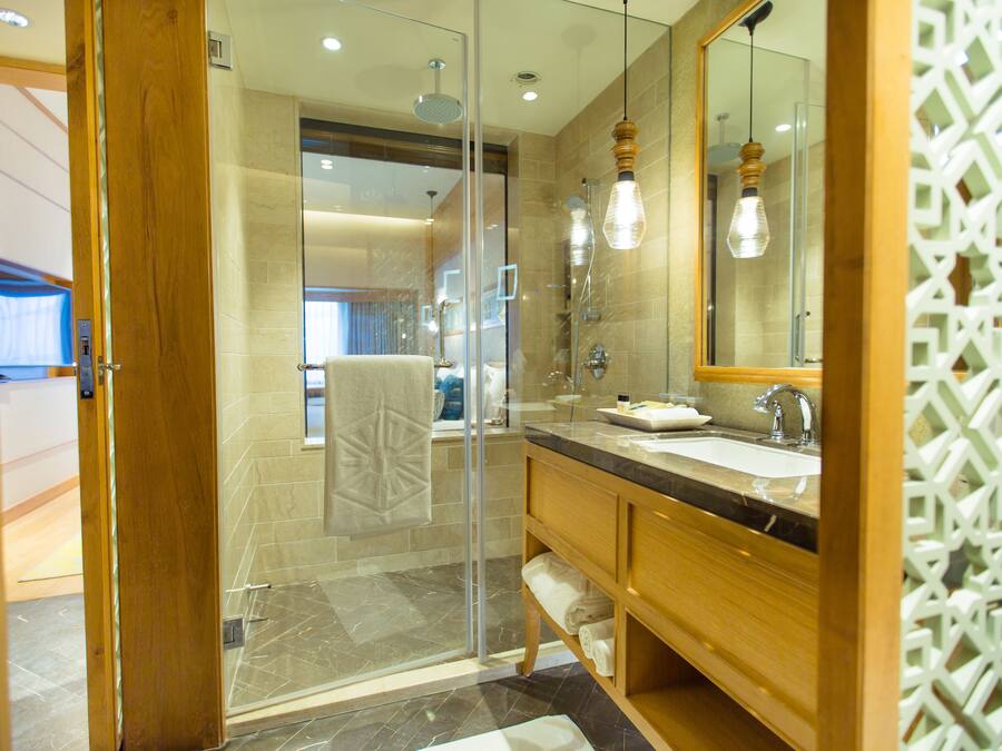 Un baño moderno con cabina de ducha de vidrio, tocador de madera con lavamanos y un espejo grande.