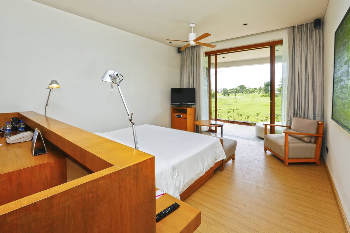 Habitación de hotel con cama, escritorio, silla, televisor y vista al exterior.
