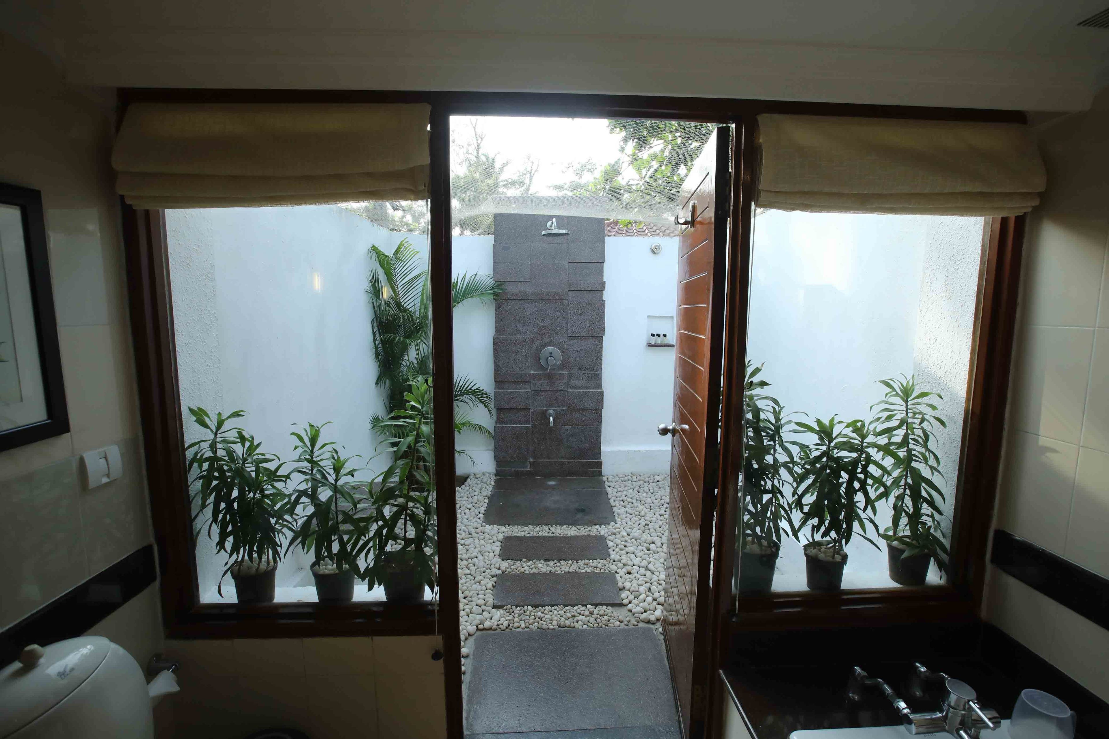 A bathroom with a shower, a toilet, and a sink. There are potted plants and a stone wall in the background.