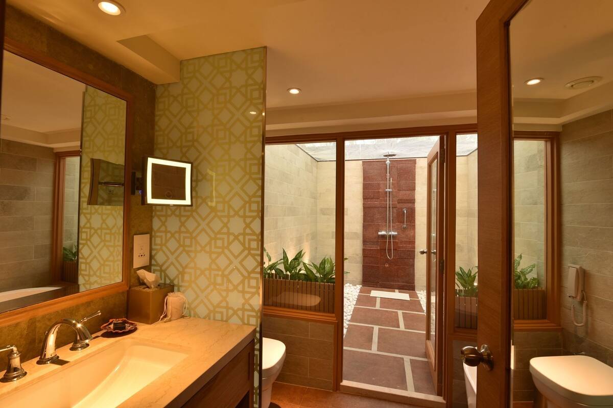 Un baño moderno con un espejo grande, dos lavamanos, una ducha y una puerta de vidrio que da a un área exterior.