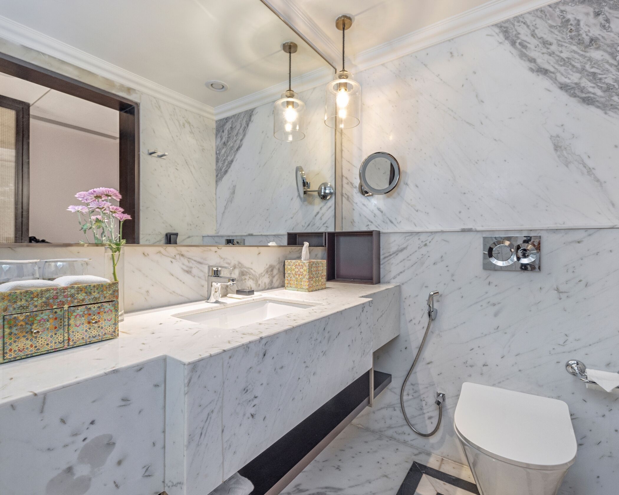 A modern bathroom with a marble countertop, a large mirror, a shower, and a toilet.