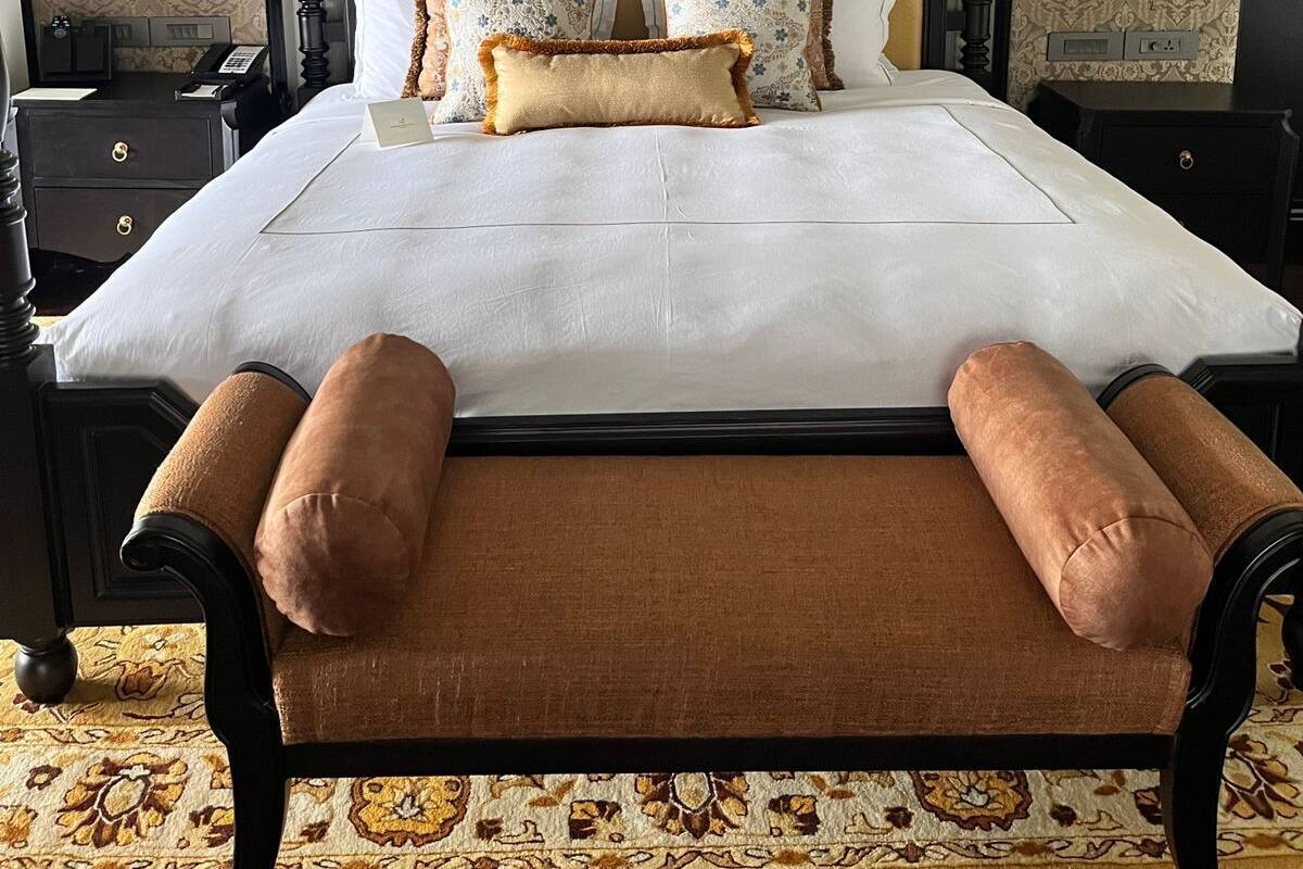 A large bed with a wooden frame, multiple pillows, and a bench at the foot.